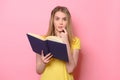 Confused cute girl thinking and reading the book on colorful pink background