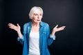 Confused elderly woman standing on black background