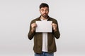 Confused and embarrassed cute indecisive caucasian male with beard, looking at blank piece paper with puzzled, hesitant
