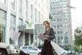 Confused female office worker throwing documents in the air near the office building. Irritated businesswoman throwing papers up