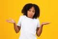 Confused funny stupid adolescent african american girl in white t-shirt, spreads arms to sides, hold copy space