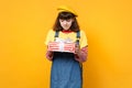 Confused girl teenager in french beret, denim sundress holding red striped present box with gift ribbon isolated on Royalty Free Stock Photo