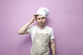 Confused guy cook in an apron scratches his head with his hand and thinks on a pink background Royalty Free Stock Photo