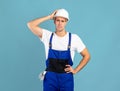Confused handyman in protective helmet and coveralls touching head in frustration