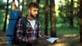 Confused hiker lost in forest tries to read map for directions, emotional stress