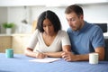 Confused interracial couple reading contract in a kitchen Royalty Free Stock Photo