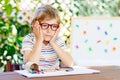 Confused little kid boy with glasses with colorful wax crayon pencils. Sad child and student is back to school Royalty Free Stock Photo