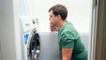 Confused man setting washing laundry machine. Male struggling and frustrating while doing housework and daily routine at Royalty Free Stock Photo