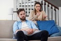 Confused man sits on the couch while his girlfriend yells and quarrels with him at home. Big family problems. Royalty Free Stock Photo
