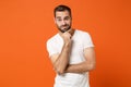 Confused pensive young man in casual white t-shirt posing isolated on orange wall background, studio portrait. People Royalty Free Stock Photo