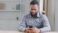 Confused puzzled angry African American ethnic bearded man boss with mobile phone reading bad news has business trouble