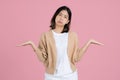 Confused puzzled upset young asian woman standing spreading hands looking at camera isolated on pastel pink colour background