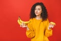 Confused sad upset curly woman can`t make a choice between healthy and unhealthy food, she is holding fruits and donut on her Royalty Free Stock Photo
