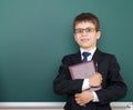 Confused school boy with book portrait, dressed in classic black suit, on green chalkboard background, education and business Royalty Free Stock Photo