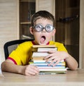 Confused schoolboy in funny glasses screaming near the huge stack of books. Education.