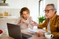 Confused senior husband and wife checking their monthly expenses, reading bills, sitting in front of laptop at kitchen Royalty Free Stock Photo