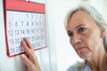 Confused Senior Woman With Dementia Looking At Wall Calendar