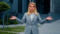 Confused serious pensive puzzled businesswoman standing outdoors spreads arms shrugs unsure caucasian woman doesn't