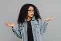 Confused unaware Afro woman with crisp hair, raises hands in bewilderment, looks aside, cannot make decision, wears spectacles and