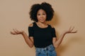 Confused unaware Afro woman with wavy curly hair, raises hands in bewilderment