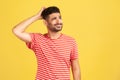 Confused uncertain man with beard in red striped t-shirt scratching his head, choosing, trying to make right decision, dilemma