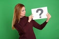 Confused woman holding question mark sign on green background Royalty Free Stock Photo