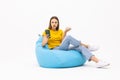 Confused woman sitting on beanbag chair and typing phone isolated on white background Royalty Free Stock Photo