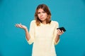 Confused woman in sweater holding smartphone and shrugs her shoulder