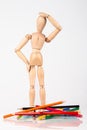 Confused wood mannequin standing at heap of colour pencil isolated on white