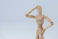 Confused wooden figurine standing with hand on head