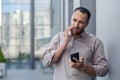 Concerned young businessman talking on smartphone and holding another phone with puzzled expression in urban setting Royalty Free Stock Photo