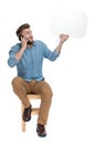 Confused young man talking on the phone and holding speech bubble Royalty Free Stock Photo