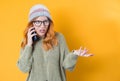 Confused young woman holding the phone, isolated on yellow background. Female person with smartphone. Nuisance concept