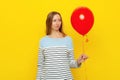 Confused young woman holds red inflated helium balloon, feels embarrassed and offended has bad mood during celebration. Holiday Royalty Free Stock Photo