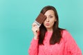 Confused young woman in knitted pink sweater holding in hand, covering eye with chocolate bar isolated on blue turquoise Royalty Free Stock Photo