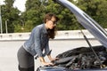 Confused young woman looking at broken down car engine on street Royalty Free Stock Photo