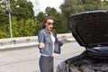 Confused young woman looking at broken down car engine on street Royalty Free Stock Photo