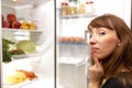 Confused young woman looking in fridge