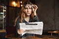 Confused young woman sitting in cafe indoors reading newspaper Royalty Free Stock Photo