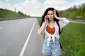 Confused young woman standing along road, feeling lost, calling on smartphone, checking travel options outdoors