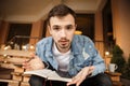 A confused young writer is looking at the camera, he is holding a notebook and a pen. He is sitting on a cafe terrace Royalty Free Stock Photo