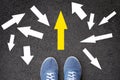 Confusing direction arrows on asphalt ground, feet and shoes on floor, personal orientation concept Royalty Free Stock Photo