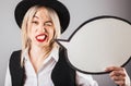 Confusing doubting skeptical woman in black hat and red lips holding speech buble blank. Royalty Free Stock Photo