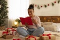 Congratulation with xmas holidays. Happy black lady reading greeting card and receiving gift boxes, sitting on bed Royalty Free Stock Photo