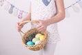 Congratulations on happy Easter: the girl is holding a basket with painted eggs by the white wall. Royalty Free Stock Photo