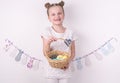Congratulations on happy Easter: the girl is holding a basket with painted eggs by the white wall. Royalty Free Stock Photo
