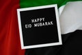 Congratulations with text HAPPY EID MUBARAK - happy holidays waving UAE flag on background concept. Greeting card Royalty Free Stock Photo