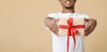 Smiling young african american man in white t-shirt giving gift box with present with red ribbon Royalty Free Stock Photo