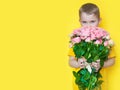 A boy in yellow clothes is holding a large bouquet of roses and a gift. Yellow background Royalty Free Stock Photo