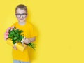 A boy in yellow clothes is holding a large bouquet of roses and a gift. Yellow background Royalty Free Stock Photo